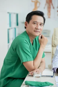 terapeuta-asiatico-vistiendo-uniforme-verde-sentado-en-el-escritorio-mirando-la-camara-retrato